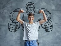 Young Caucasian boy in white t-shirt showing biceps muscles with superhero shadow drawing on grey wall background representing strength, dreams and aspirations.