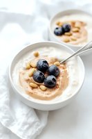 Creamy yogurt bowl topped with fresh blueberries, pine nuts and cinnamon swirl on white background, served in ceramic dish. Healthy breakfast concept.