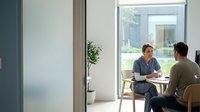 Healthcare professional consulting with male patient in modern medical office setting with natural lighting and contemporary furniture.