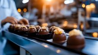 Artisanal chocolate truffles on dark surface with bokeh lights in background, confectioner preparing luxury handmade pralines in professional kitchen.