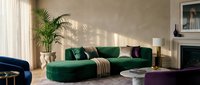 Modern living room with curved green velvet sectional sofa, natural sunlight, potted palm plant, and contemporary home decor for interior design projects.
