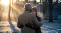 Senior couple embracing in winter park during golden hour sunset. Elderly man and woman sharing tender moment outdoors in snowy landscape for romance concepts.