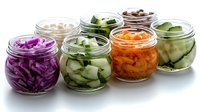 Assorted fermented and pickled vegetables in glass jars including purple cabbage, cucumbers, and carrots. Fresh homemade probiotics for gut health.