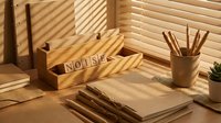 Wooden desk organizer with pencil holder and letter tiles spelling NOISE on sunlit workspace with venetian blind shadows creating striped light patterns.