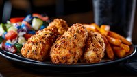 Crispy breaded chicken cutlets served with roasted carrots and fresh garden salad on black plate, close up view of homestyle comfort food dinner.