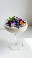 Chia seed pudding topped with fresh blueberries, raspberries and edible flowers in elegant glass bowl for healthy breakfast or dessert presentation.