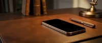 Modern smartphone with stylish pen on wooden desk in warm office setting with vintage books and brass lamp creating professional workspace atmosphere.