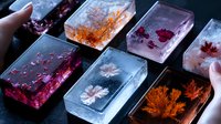 Handmade resin art pieces with preserved flowers and leaves in rectangular shapes, creating luminous decorative objects in purple, orange, and blue tones.