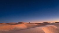 A lone vehicle traverses vast golden sand dunes under a starlit twilight sky, capturing desert adventure and remote travel exploration.
