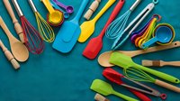 Colorful kitchen utensils and cooking tools arranged on turquoise background. Silicone spatulas, wooden spoons, whisks and measuring cups for culinary preparation.