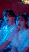 Young Asian couple in white clothing illuminated by dramatic blue neon lighting against dark background, creating moody atmospheric nightclub scene.