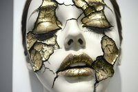 Dramatic close up of white porcelain face with cracked gold leaf texture peeling away to reveal layers beneath, creating an artistic beauty concept for makeup and fashion.