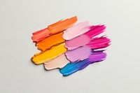 Vibrant makeup swatches in gradient colors from orange to blue create dynamic brush strokes on white background, showcasing cosmetic texture and pigmentation.