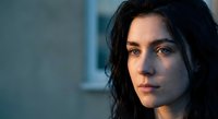 Young brunette woman with wet hair looking pensively at camera in soft blue light. Moody portrait with emotional expression for wellness and beauty concepts.