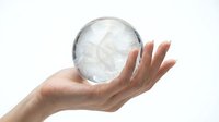 Hand holding transparent crystal ball sphere with reflections on white background for fortune telling and mystical concepts.