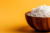 Wooden bowl filled with cooked white rice on bright yellow background, suitable for food blogs, cooking websites, recipe content, and culinary publications.