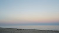 Serene beach sunset with soft pastel sky colors reflecting on calm ocean water, empty sandy shore with driftwood, peaceful coastal evening atmosphere.