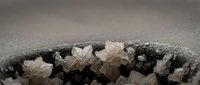 White salt crystals forming geometric cubic structures on dark mineral surface with crystalline formations and natural texture patterns.
