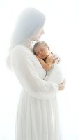 Tender mother in white dress holding sleeping newborn baby in soft natural light creating peaceful maternal bonding moment for family photography.
