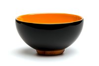 Modern black ceramic bowl with bright orange interior and wooden base, minimalist Asian-inspired design for contemporary dining and home decor styling.