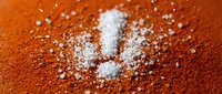White sea salt crystals scattered on vibrant orange paprika powder creating culinary seasoning contrast for cooking and food preparation.