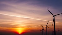 Wind turbines silhouetted against dramatic sunset sky with orange and purple clouds. Renewable energy concept for sustainable power generation projects.