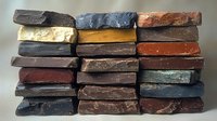 Stacked artisanal soap bars in natural earth tones and textures create rustic pattern. Handmade organic cosmetic products arranged in rows showing variety of colors.