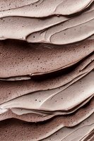 Creamy chocolate frosting texture with smooth swirls and delicate air bubbles creating waves of rich brown dessert topping. Macro food photography background.