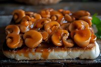 Caramel glazed mushrooms arranged on toasted bread slice create rich appetizer with golden brown toppings and glossy sauce on rustic wooden surface.