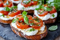 Toasted bread slices topped with fresh mozzarella, cherry tomatoes, and basil leaves, drizzled with olive oil and herbs served on dark stone background.