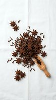 Star anise and cloves scattered from wooden scoop on white marble surface for culinary and aromatherapy applications.