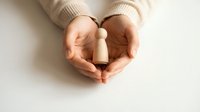 Hands gently cupping wooden cylinder object in protective gesture on clean white surface for mindfulness meditation wellness concepts.