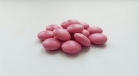 Pink candy-coated almonds piled on a white surface, sweet sugared nuts in pastel rose color, perfect for confectionery and food styling concepts.