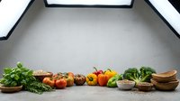 Fresh organic vegetables and herbs arranged on wooden bowls and cutting boards in modern kitchen setting for healthy cooking and meal preparation.
