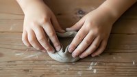 Hands kneading dough on wooden surface for homemade bread baking and cooking preparation in kitchen.