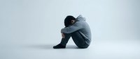 Young Asian man sitting alone in fetal position expressing depression, anxiety and mental health struggles on white background for design use.