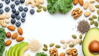 Healthy superfood ingredients frame with nuts, seeds, berries, avocado and leafy greens on white background for nutritious meal planning and wellness.
