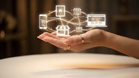 Businesswoman holding glowing digital network of connected smart home devices and technology icons above palm, representing IoT connectivity and home automation solutions.
