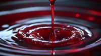Red liquid droplet creating concentric ripples and splash crown on dark reflective surface with dramatic lighting, captured in high-speed macro photography.