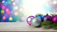 Festive Christmas ornaments in purple, blue, and silver with pine branches on wooden surface against colorful bokeh background.