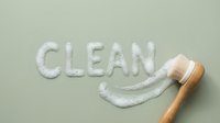 Cleaning product with wooden brush creating smiley face on sage green surface, hygiene and household cleaning concept for marketing and advertising purposes.