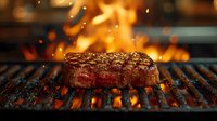 Juicy beef steak grilling on flaming barbecue grill with fire and sparks in background, close up view of meat cooking on hot grate surface.