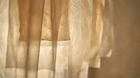 Sheer beige curtains with soft natural light filtering through fabric folds, creating elegant shadows and warm tones suitable for interior design and home decor projects.