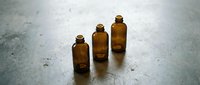 Three amber glass bottles of varying sizes arranged in ascending order on a textured concrete surface, suitable for pharmaceutical, cosmetic, or essential oil product packaging mockups.