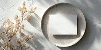 Blank card on ceramic plate with dried pampas grass, creating minimal aesthetic composition with soft shadows on white textured background.