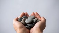 Hands holding smooth gray stones against white background, representing care, wellness, meditation, and natural healing practices.