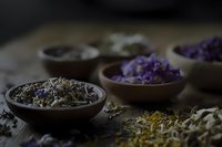Aromatic dried herbs and flowers in rustic wooden bowls on dark textured surface, moody lighting creates mystical atmosphere for natural wellness and herbal medicine.