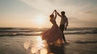 Romantic couple dancing on beach at sunset, silhouetted against golden sky. Woman in flowing dress twirls with male partner as waves crash on shore. Dreamy atmospheric beach wedding scene.