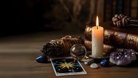 Mystical fortune telling setup with tarot cards, burning candle, crystals and ancient books on wooden table creating atmospheric divination scene.