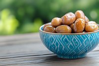 Fresh dates in decorative turquoise ceramic bowl on rustic wooden table against blurred green garden background, healthy Middle Eastern snack.